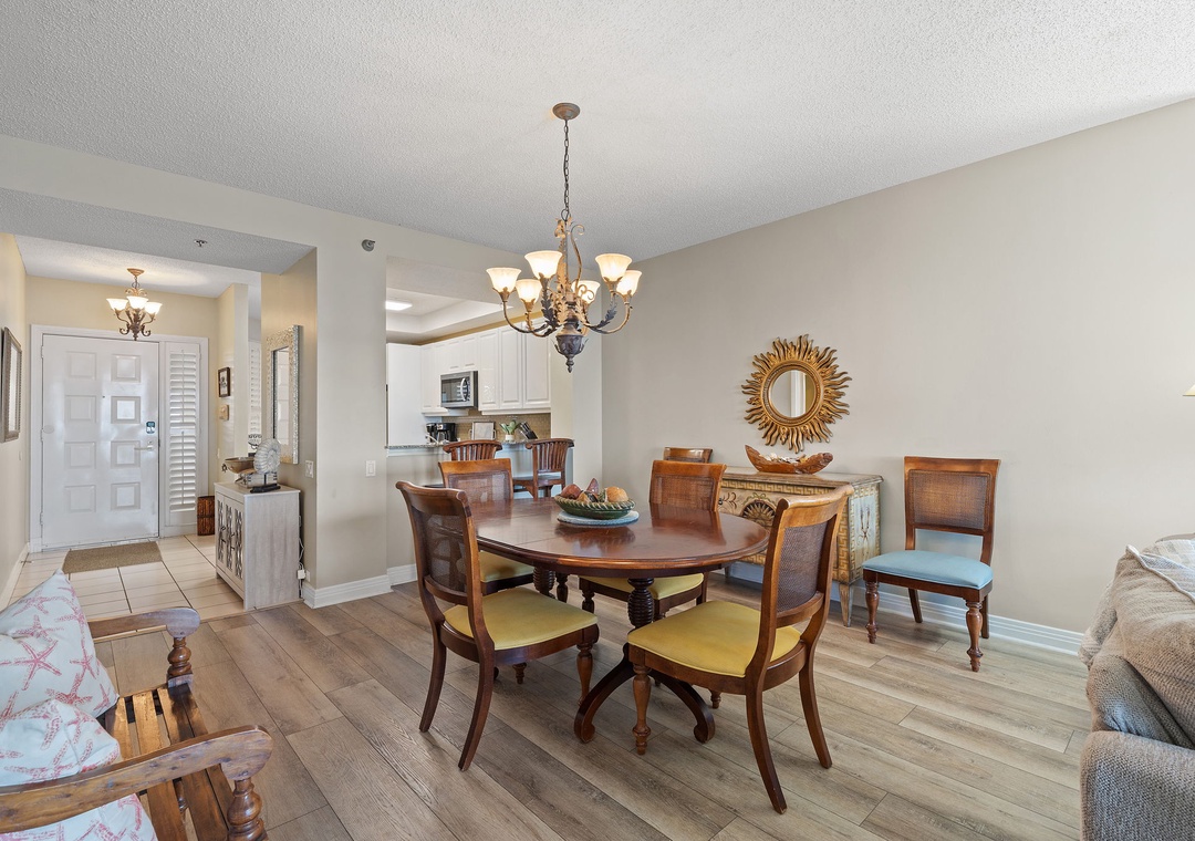 Beach Colony T15B- Step into your inviting dining area with warm wood floors and elegant furnishings. Gather around the oval table under soft chandelier light, with your open kitchen just steps away for easy entertaining.