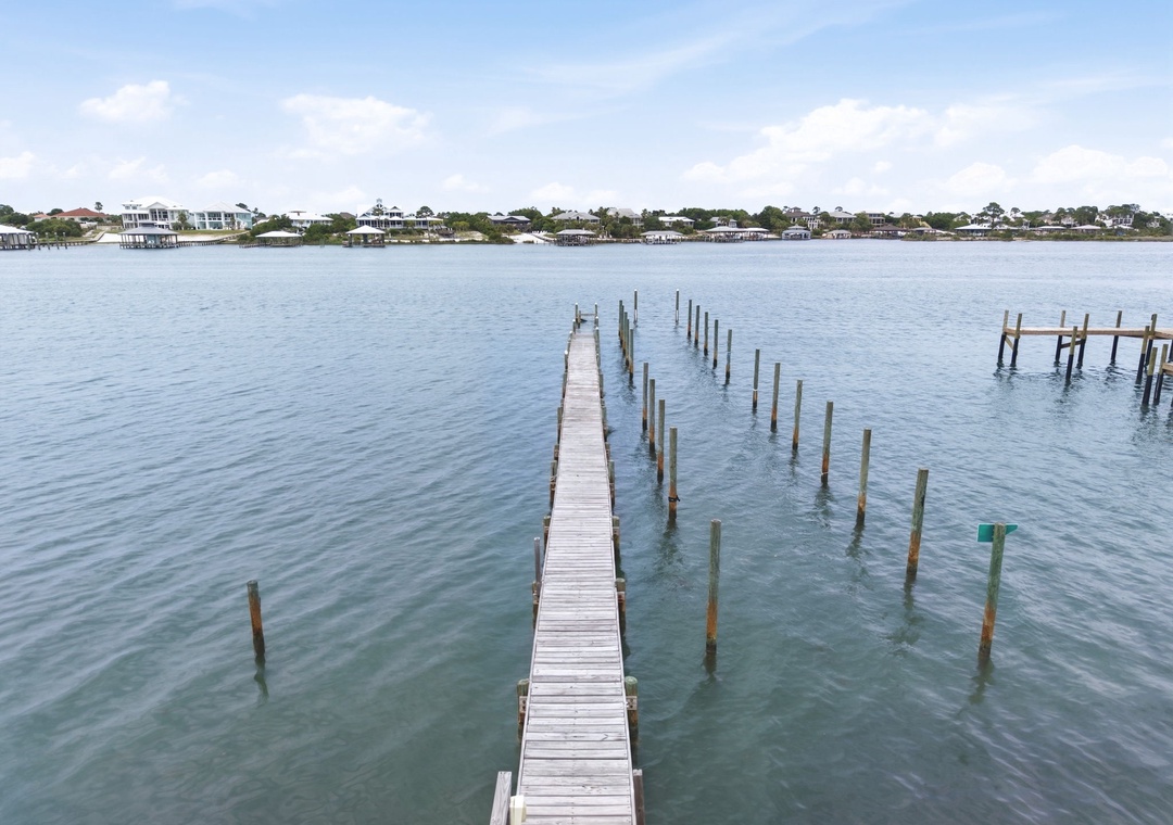 A private dock extends into calm coastal waters, offering easy access to waterfront activities. The serene bay and neighboring homes create a peaceful waterside community setting.