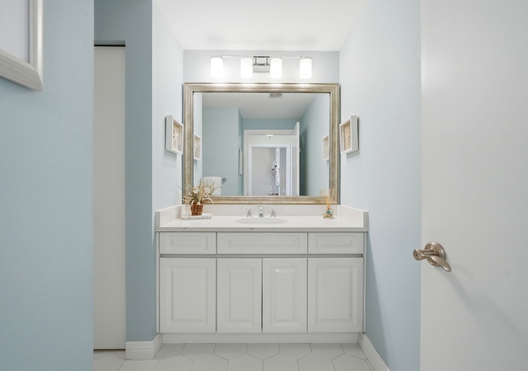 Beach Colony Tower PH1B -Step into your serene bathroom retreat, where soft blue walls frame a pristine vanity with crisp white cabinets, a gleaming mirror, and elegant fixtures—your perfect space to refresh and unwind.