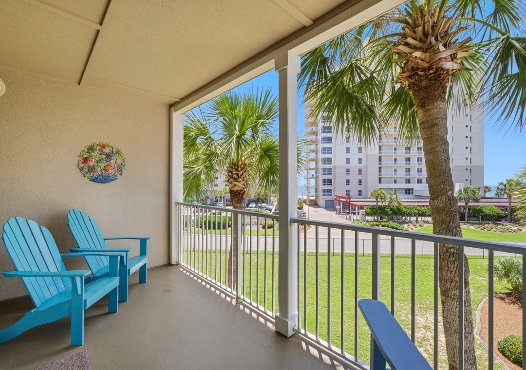 Grand Caribbean 305W- Relax in comfort on your private balcony, where vibrant blue chairs frame views of swaying palms and coastal charm—perfect for sipping morning coffee.