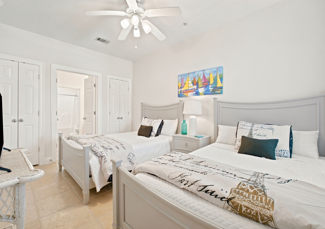Your coastal-inspired bedroom awaits with two plush beds dressed in seaside linens, a gentle ceiling fan overhead, and a splash of sailboat art to carry you away to peaceful dreams.