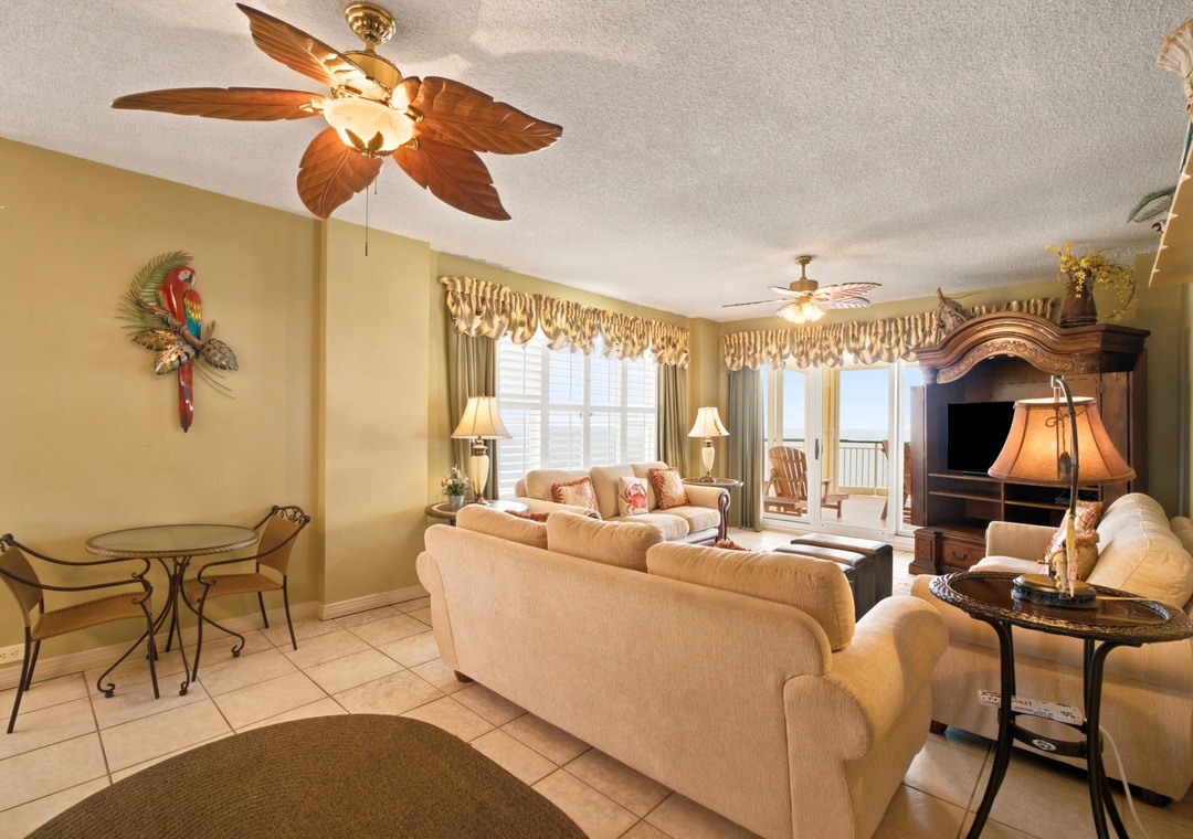 Beach Colony W13A- Relax in your comfortable living space with tropical-themed décor, ceiling fan, entertainment center, and access to your private balcony with views beyond.