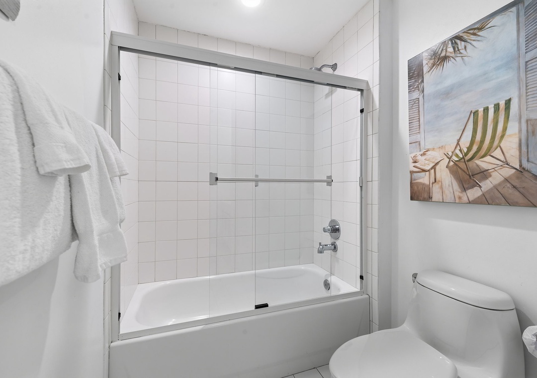 Beach Colony T14B- A pristine bathroom awaits with crisp white tiles, a refreshing tub-shower combo, and plush towels ready for your arrival.