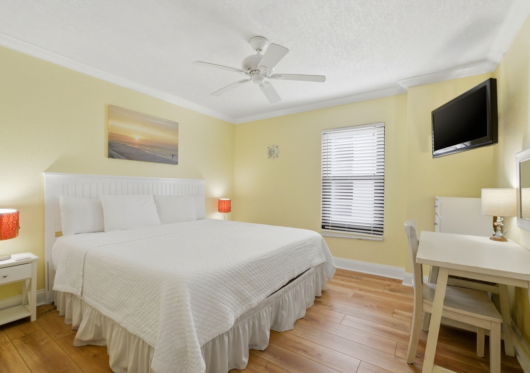 Ocean Breeze E601- Cheerful, sunlit retreat features a plush bed dressed in crisp linens, calming artwork, and modern amenities like a flat-screen TV and desk. Warm wood floors and gentle breezes from the ceiling fan make this space perfect for unwinding.