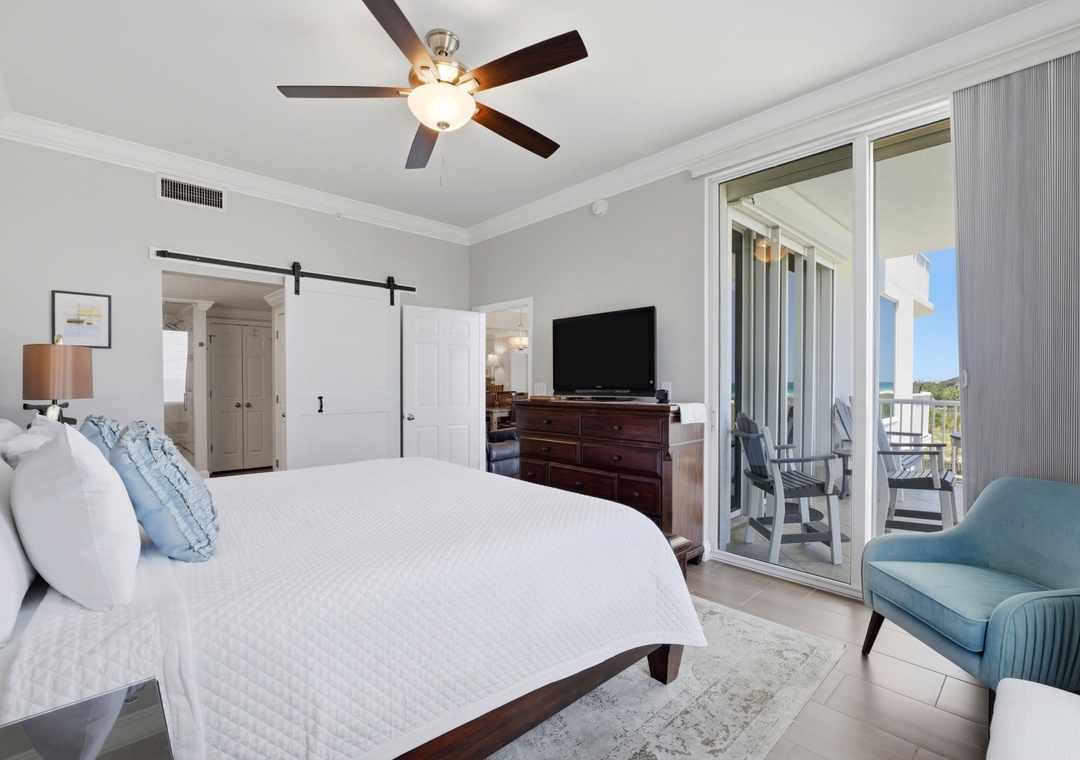 Step into this serene coastal bedroom with crisp linens, a cozy seating nook, and balcony doors opening to peaceful water views—your perfect retreat awaits.