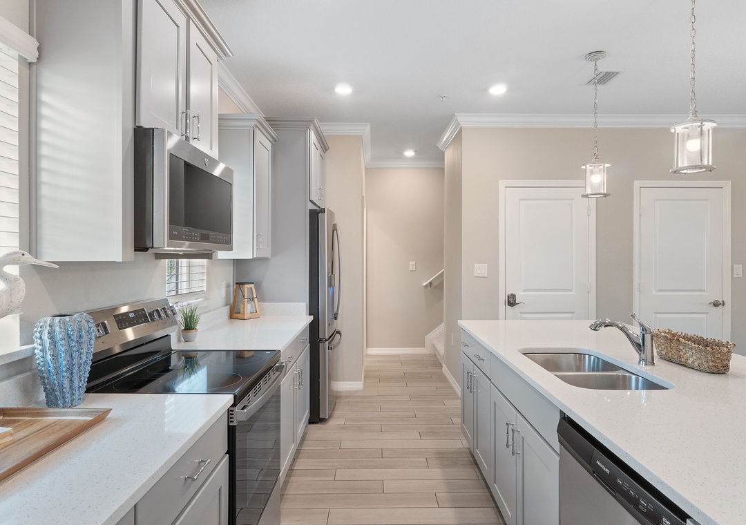 Saltwater & Sunsets- Your gourmet kitchen awaits, featuring sleek gray cabinetry, stainless steel appliances, and bright quartz countertops—perfect for preparing memorable meals and gathering with loved ones.