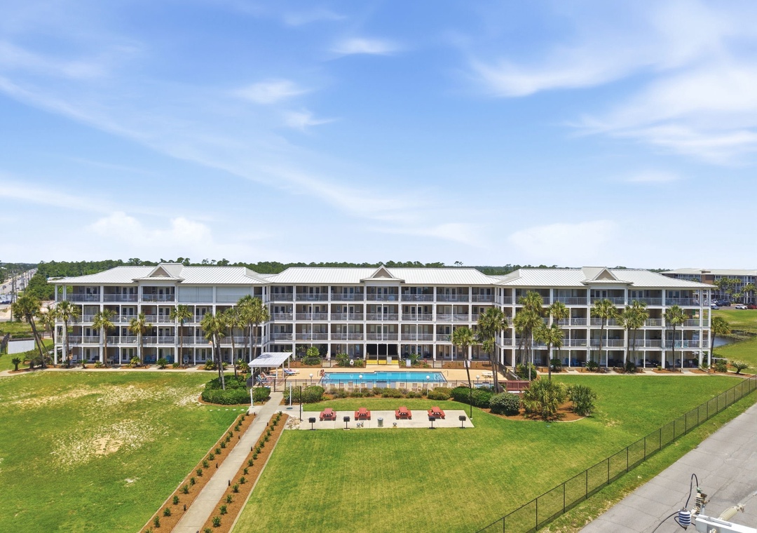 Grand Caribbean -Coastal resort property featuring multi-story buildings with private balconies, landscaped grounds with palm trees, and an outdoor pool surrounded by tropical greenery.