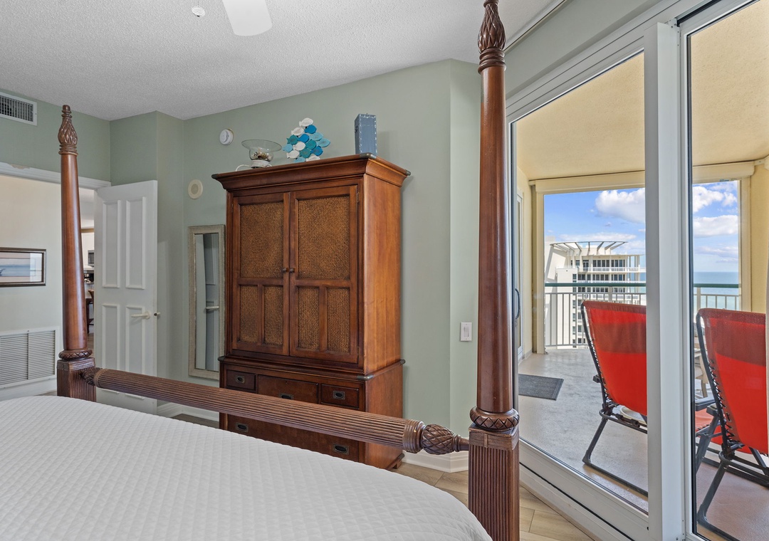 Beach Colony T15B- Your coastal retreat features a plush bed with carved wooden posts and a balcony with ocean views, creating a tranquil space to unwind after beach days.