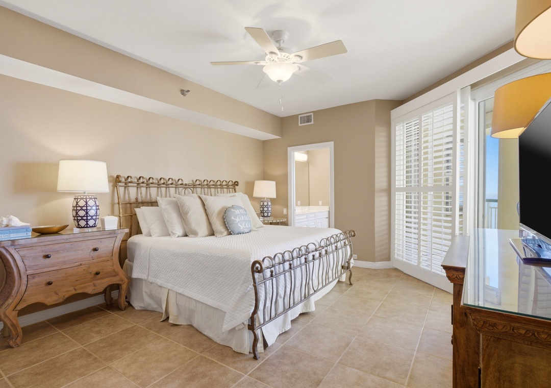 Beach Colony T PH1D- Your coastal retreat features a plush bed, warm lighting, and ocean breezes flowing through plantation shutters. Ceiling fan above keeps you cool while you unwind in comfort.