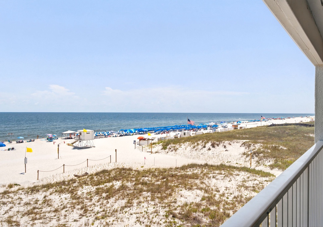 Gulfside Villas 2B- This balcony offers direct views over sandy dunes and the sparkling Gulf of Mexico, where colorful umbrellas dot the shoreline and waves invite relaxation.
