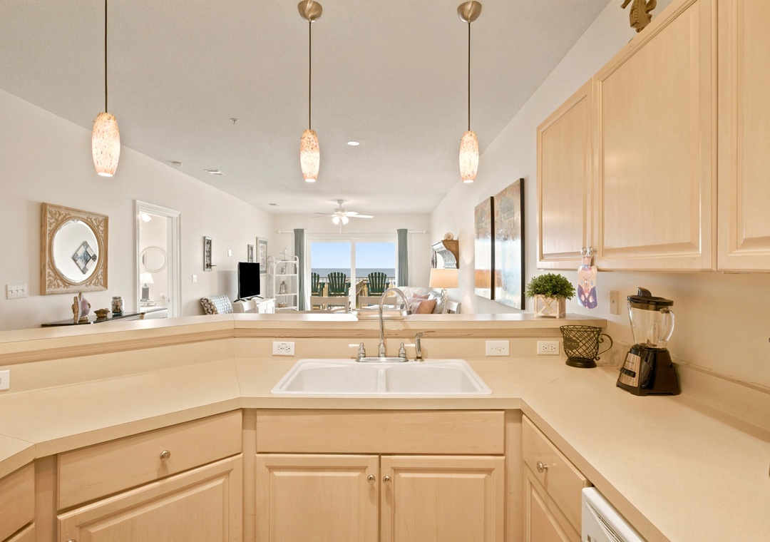 Your beautifully appointed kitchen opens to a sunlit living space, offering warm wood cabinetry, modern appliances, and elegant pendant lighting that sets the perfect tone for relaxing vacation meals.