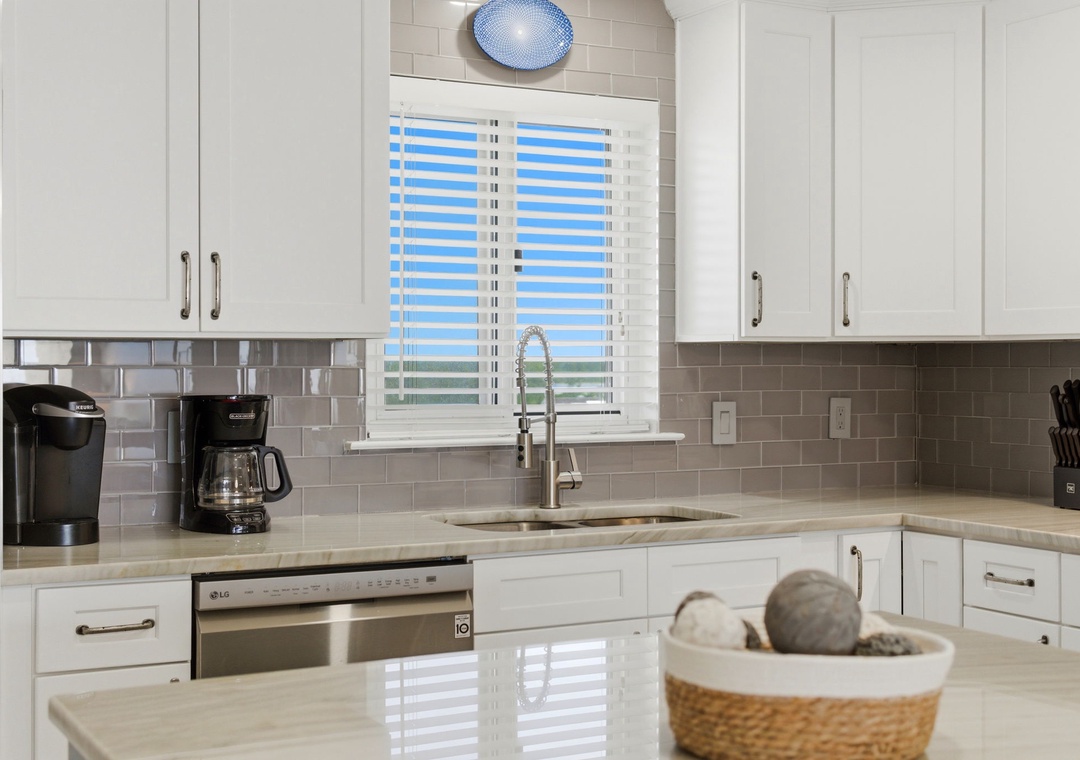 Imagine brewing your morning coffee in this bright, modern kitchen with its gleaming countertops and coastal-inspired tile. You'll love the open space and natural light streaming through.