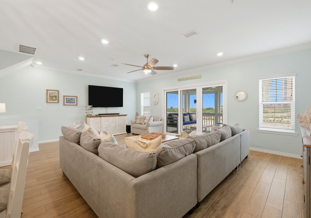 Sink into plush sofas as natural light pours through glass doors, offering a peaceful balcony view. Enjoy cozy evenings with entertainment and coastal charm all around you.
