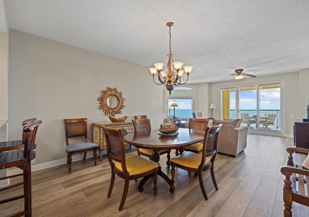 Beach Colony T15B- Gather around the elegant dining table while sunlight streams through the balcony doors, framing stunning ocean views. This open space flows seamlessly from dining to living, perfect for memorable meals and easy conversations.