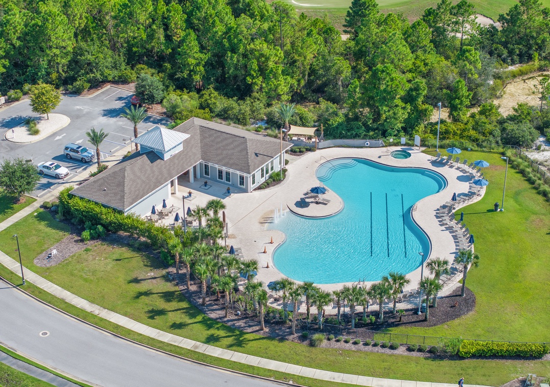 Lost Key Community Aerial view showcasing the large freeform swimming pool with adjacent clubhouse, surrounded by lush landscaping and bordered by a golf course. The community amenity area includes ample parking and is nestled among towering trees.