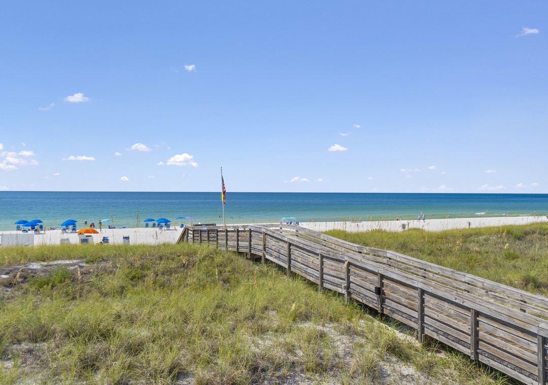 The Lost Key Beach Club The wooden boardwalk leads to pristine white sands and turquoise waters, where beach chairs and umbrellas await under clear blue skies.