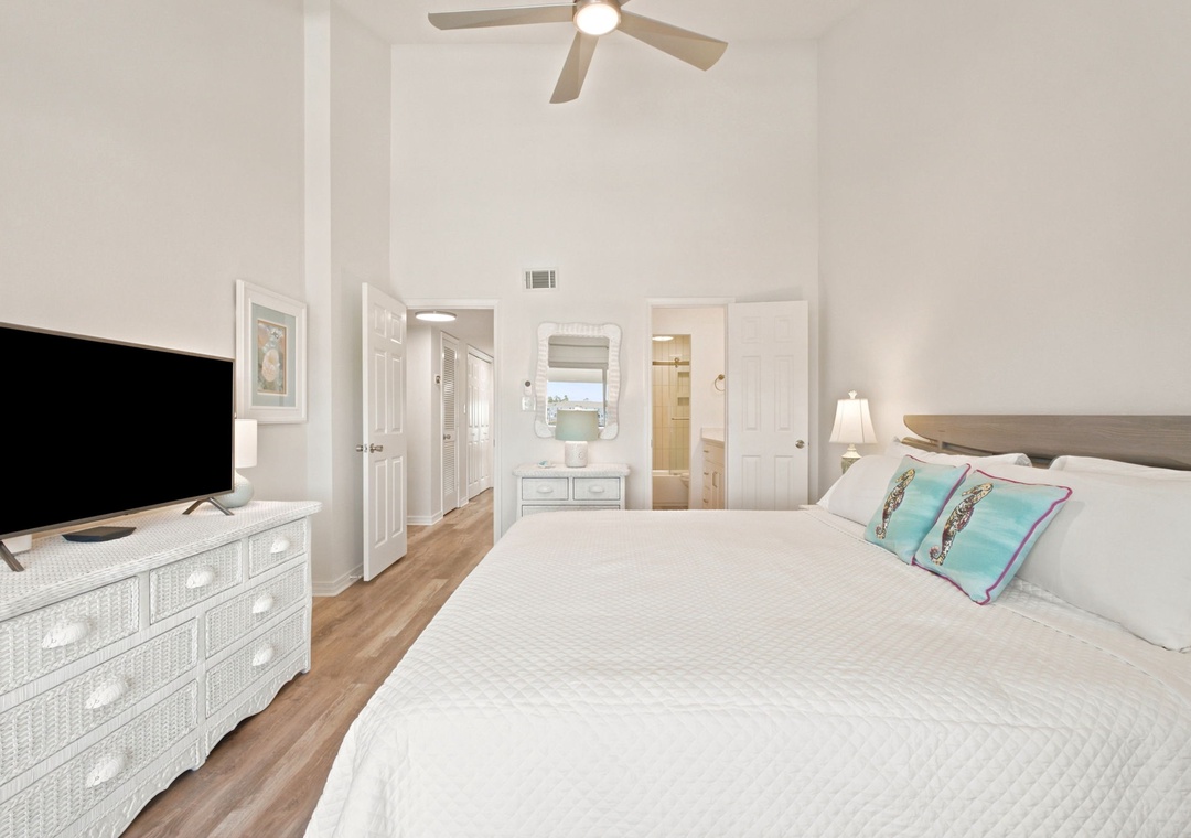Gulfside Villas 2B- Unwind in your serene bedroom with vaulted ceilings, coastal decor, and a ceiling fan keeping you cool. Your private ensuite awaits through the door.
