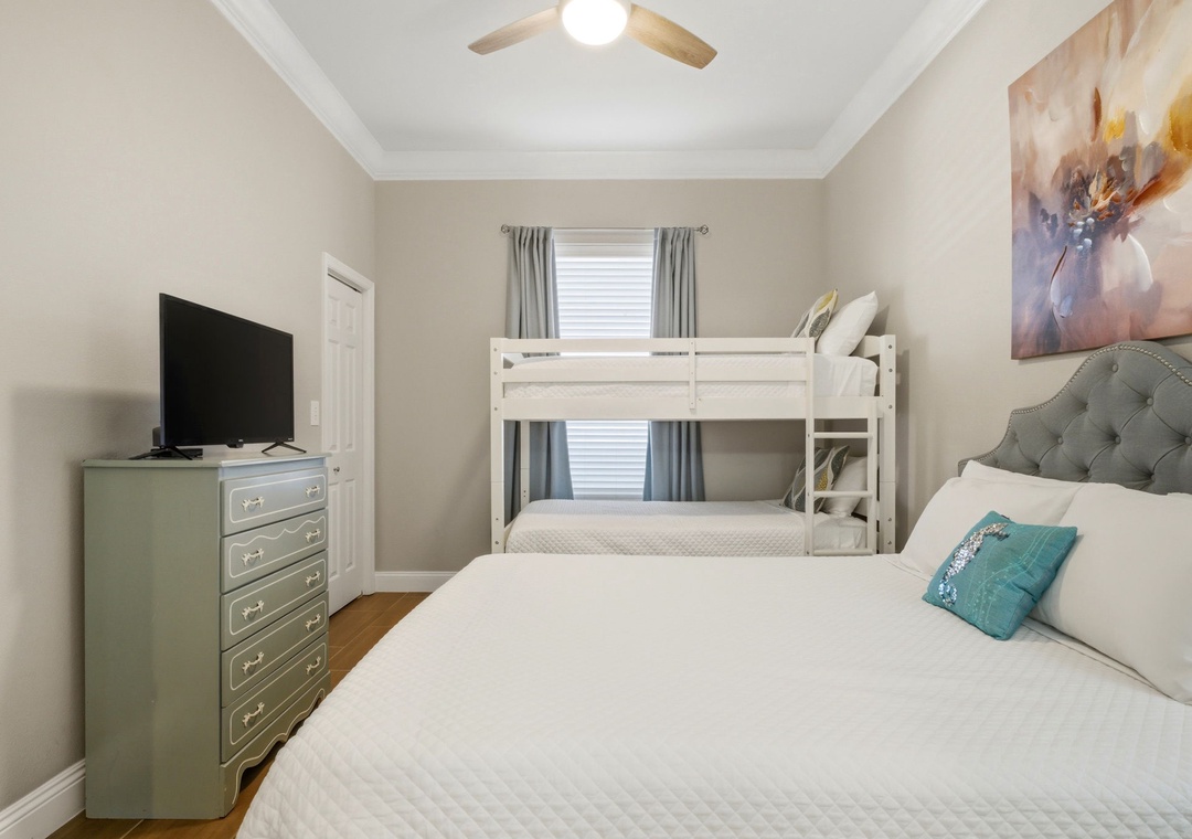 Unwind in your serene bedroom, featuring a plush queen bed and bunk beds for extra guests. Soft linens, gentle artwork, and a ceiling fan ensure your comfort.