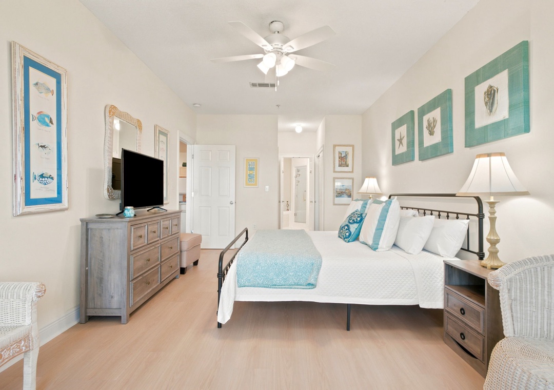 Your coastal-inspired retreat awaits with a plush bed dressed in soothing aqua linens, beach-themed artwork, and ceiling fan keeping you comfortable year-round.