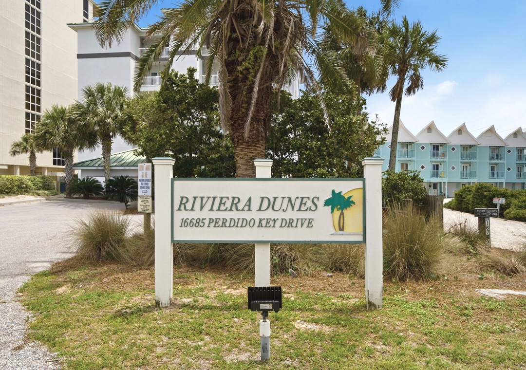 Riviera Dunes entrance sign at 16685 Perdido Key Drive, located in a tropical coastal neighborhood with palm trees and nearby beachfront access.