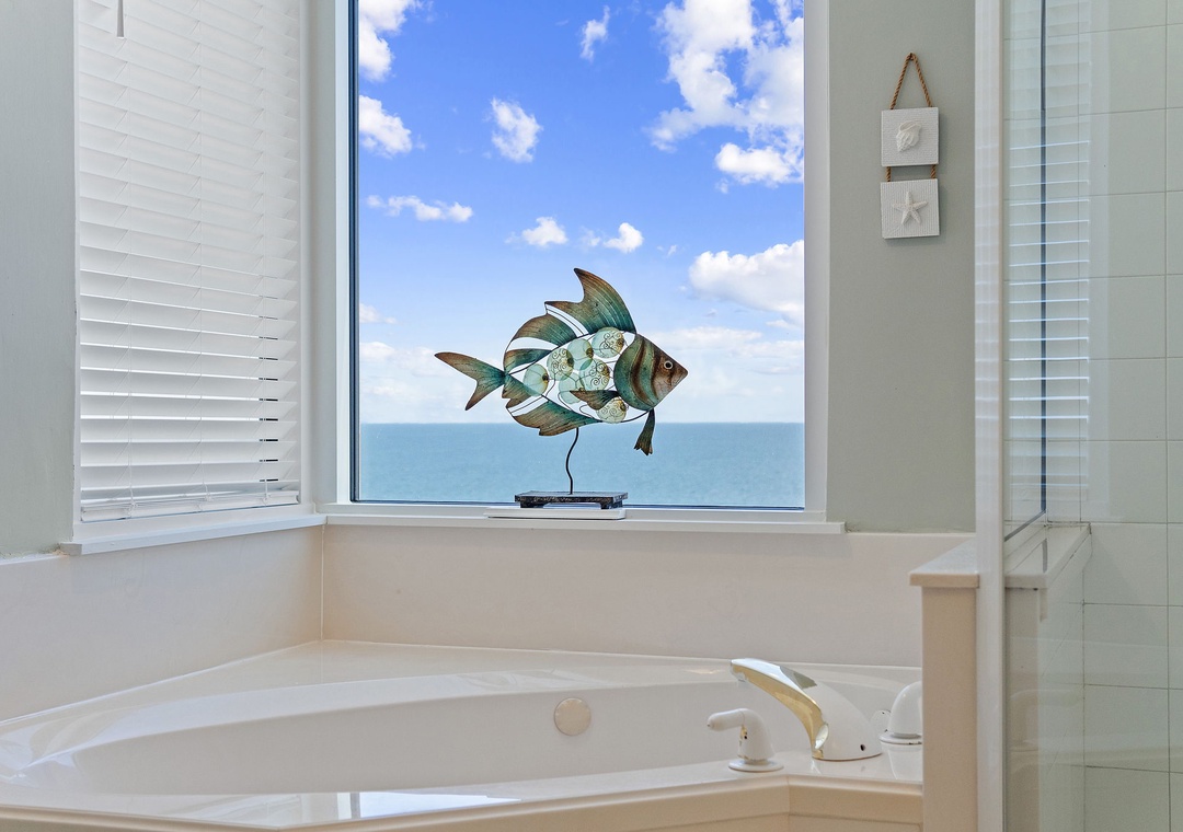 Beach Colony T15B- Soak in the tub while taking in stunning ocean views through the large window, where blue skies meet gentle waves on the horizon.