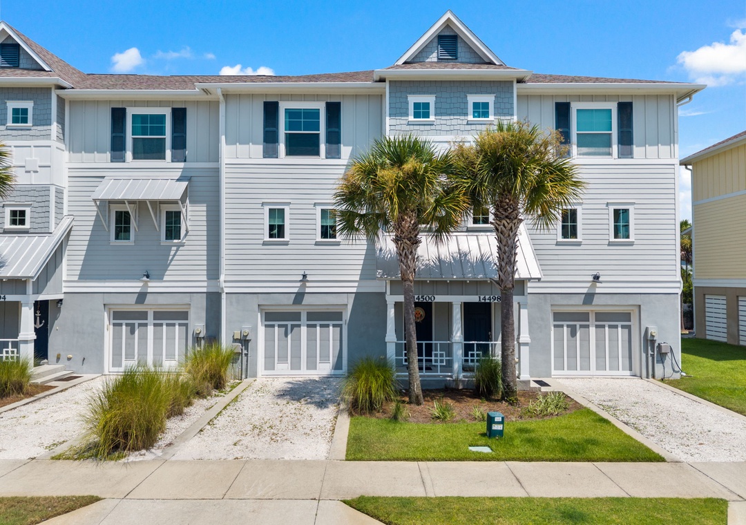 Turtles Nest- Modern coastal townhome exterior featuring tropical landscaping and a bright blue sky, located in a tranquil residential neighborhood.