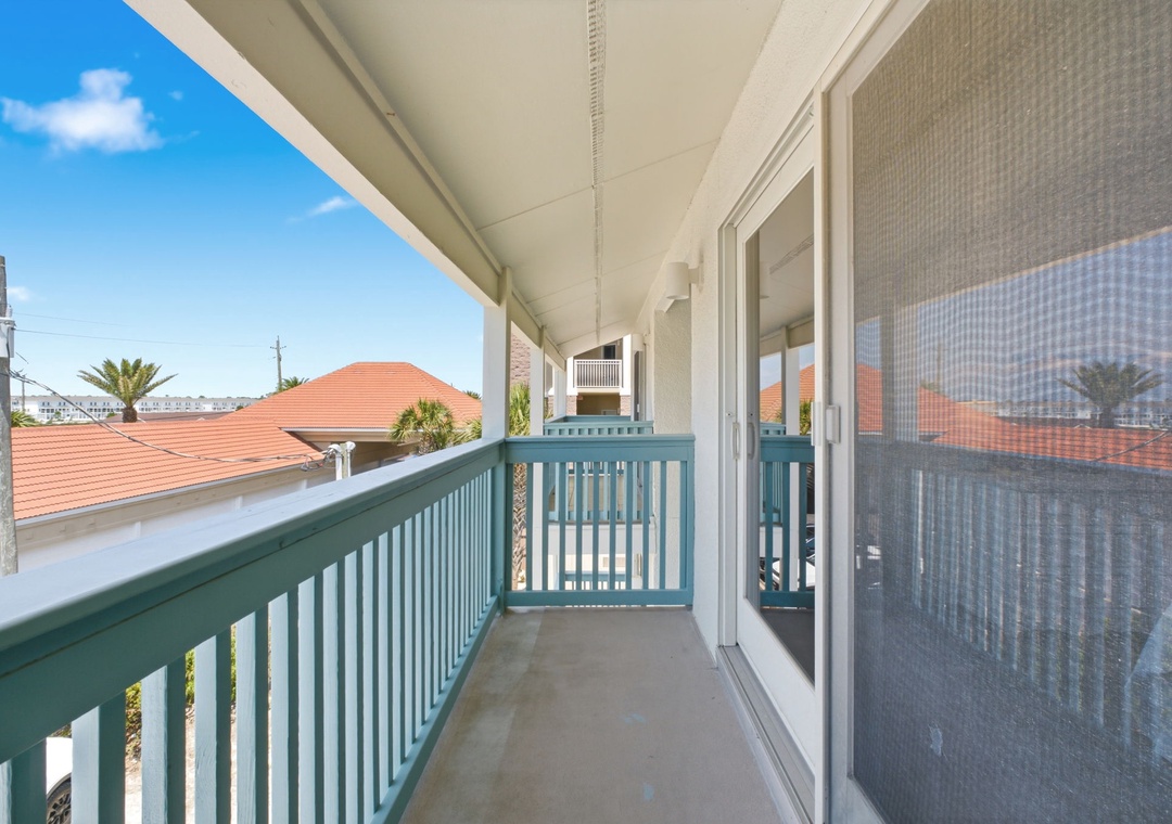 Gulfside Villas 2B- Covered balcony showcasing rooftop views and blue skies in a peaceful residential setting, providing a comfortable outdoor space to enjoy the neighborhood surroundings.
