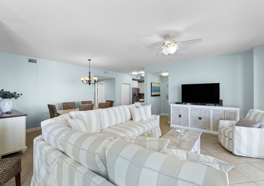 Beach Colony Tower 10C- Spacious coastal retreat with soft aqua walls and plush striped sofas. Open-concept living and dining area flooded with natural light, perfect for relaxed beachside evenings.