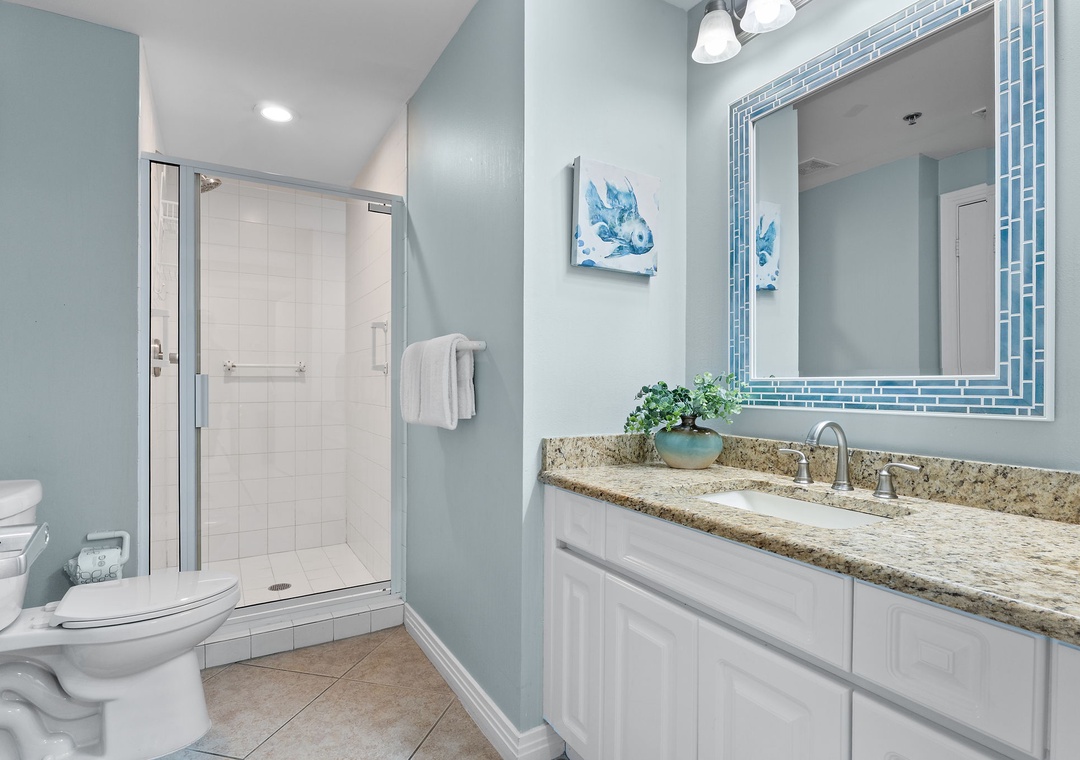 Beach Colony Tower 10C- Step into your serene coastal-themed bathroom with a spacious walk-in shower, granite vanity, and soothing blue tones that make freshening up feel like a mini spa retreat.