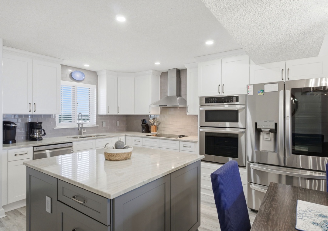 This bright, modern kitchen features gleaming white cabinetry, marble-look countertops, and stainless steel appliances—everything you need to whip up vacation meals together in style and comfort.