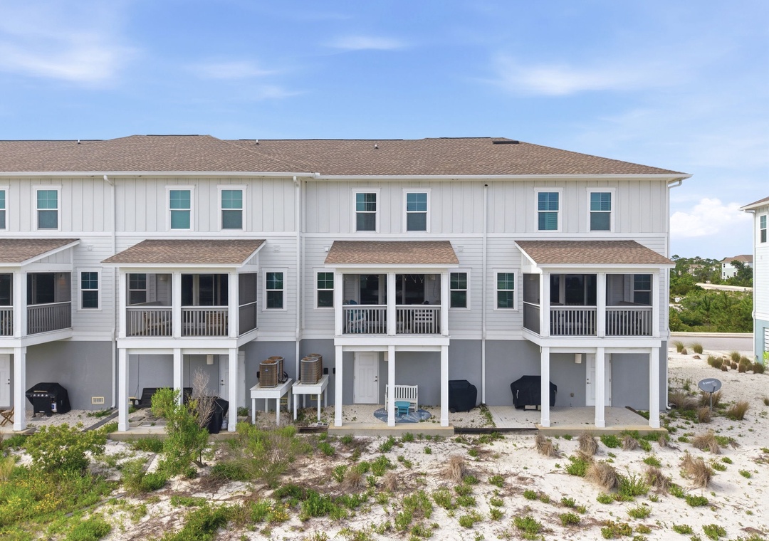 Modern beachside townhome complex featuring multiple units with covered parking and screened porches, situated steps from sandy shores in a coastal residential area.