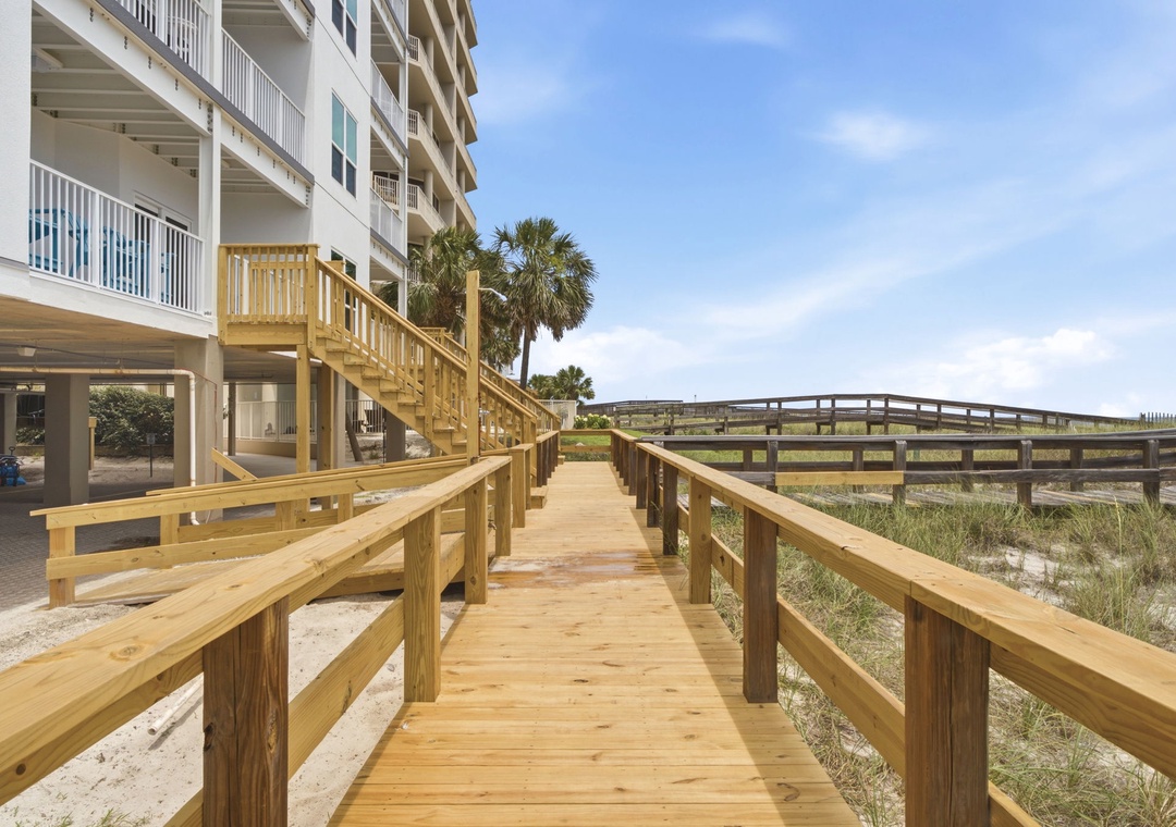 A private wooden boardwalk leads directly from the property across coastal dunes toward beach access, with palm trees swaying nearby and ocean breezes just steps away.