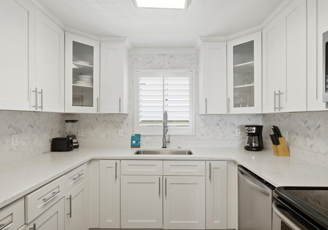 Sandy Key 827- Your bright, fully-equipped kitchen features elegant white cabinetry, marble backsplash, and stainless appliances—perfect for preparing meals with natural light streaming in.