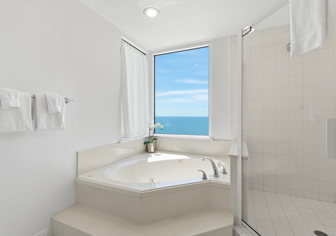 Beach Colony T14B- Unwind in your private oasis featuring a luxurious soaking tub with breathtaking ocean views and a spacious walk-in shower with sleek tile finishes.