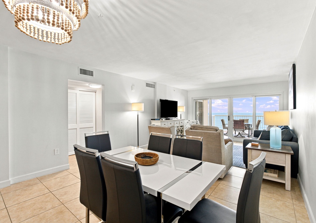 Sandy Key 411- Gather with your loved ones at the spacious dining table, where an elegant chandelier sets the mood and bright ocean views beckon from the balcony beyond.