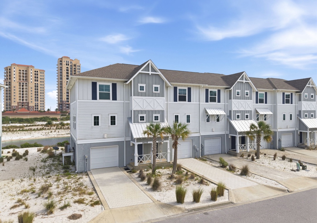 Coastal townhome community featuring modern beach architecture with private garages, nestled between sandy dunes and nearby high-rise buildings.