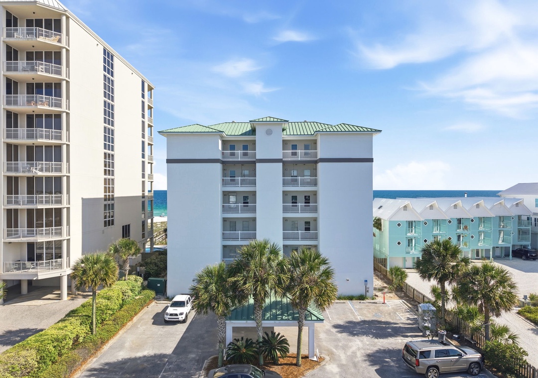 Coastal vacation rental building situated near the beach with palm-lined grounds and sea access. The property features multiple balconies and is located within a residential beachfront community.