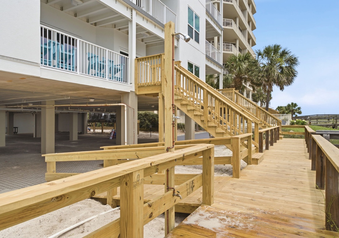 A wooden boardwalk leads past the building through coastal surroundings framed by palm trees and open blue skies.