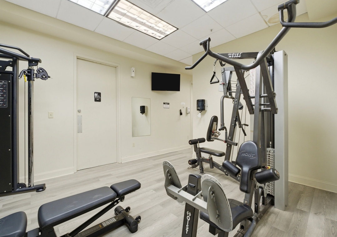 Stay active during your visit with a well-equipped fitness center featuring strength-training machines, cable systems, and free weights under natural light from skylights above.