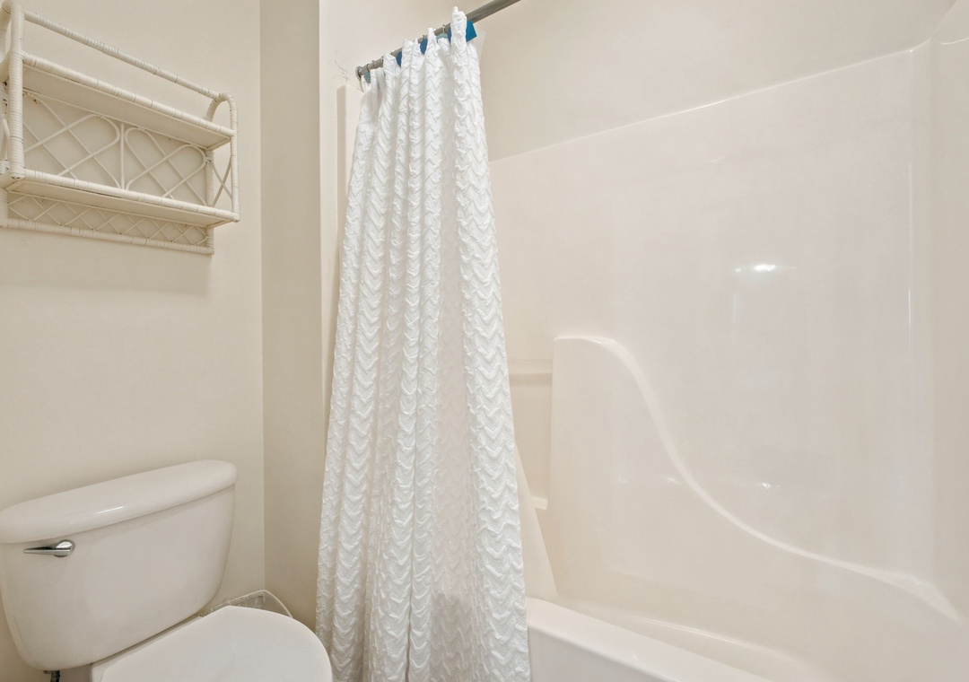 Your private bathroom features a clean shower-tub combo with fresh linens and convenient storage above the toilet—everything you need for a relaxing refresh.