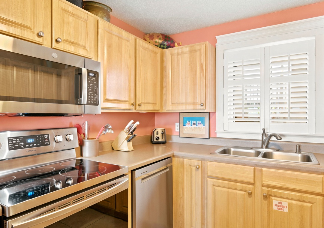 Sandy Key 338- Your fully equipped kitchen offers stainless steel appliances, warm wood cabinetry, and cheerful coral walls—perfect for preparing meals while soaking in natural light streaming through plantation shutters.