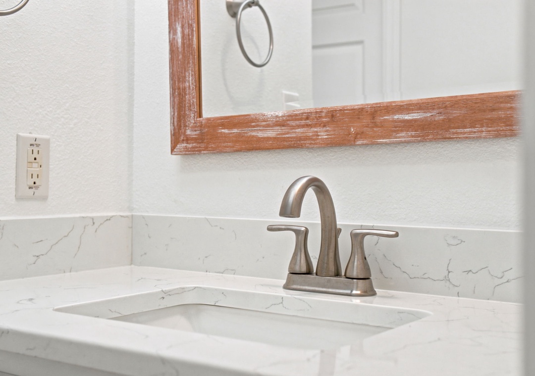 Gulfside Villas 2B- Freshen up in your beautifully updated bathroom featuring a marble-look countertop, modern brushed nickel faucet, and warm wood-framed mirror that adds coastal charm.