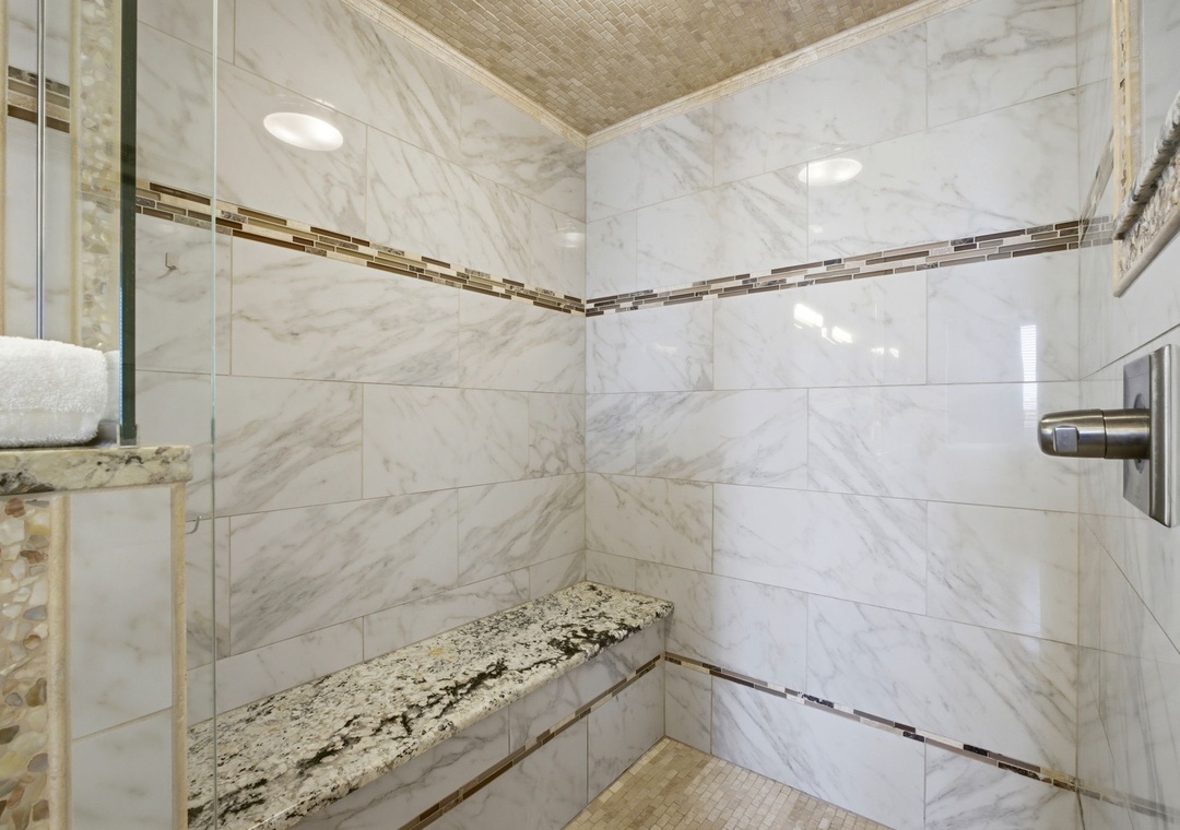 Step into your luxurious walk-in shower with elegant marble tile, granite bench seating, and a soothing rainfall ceiling. Unwind in style with designer touches at every turn.