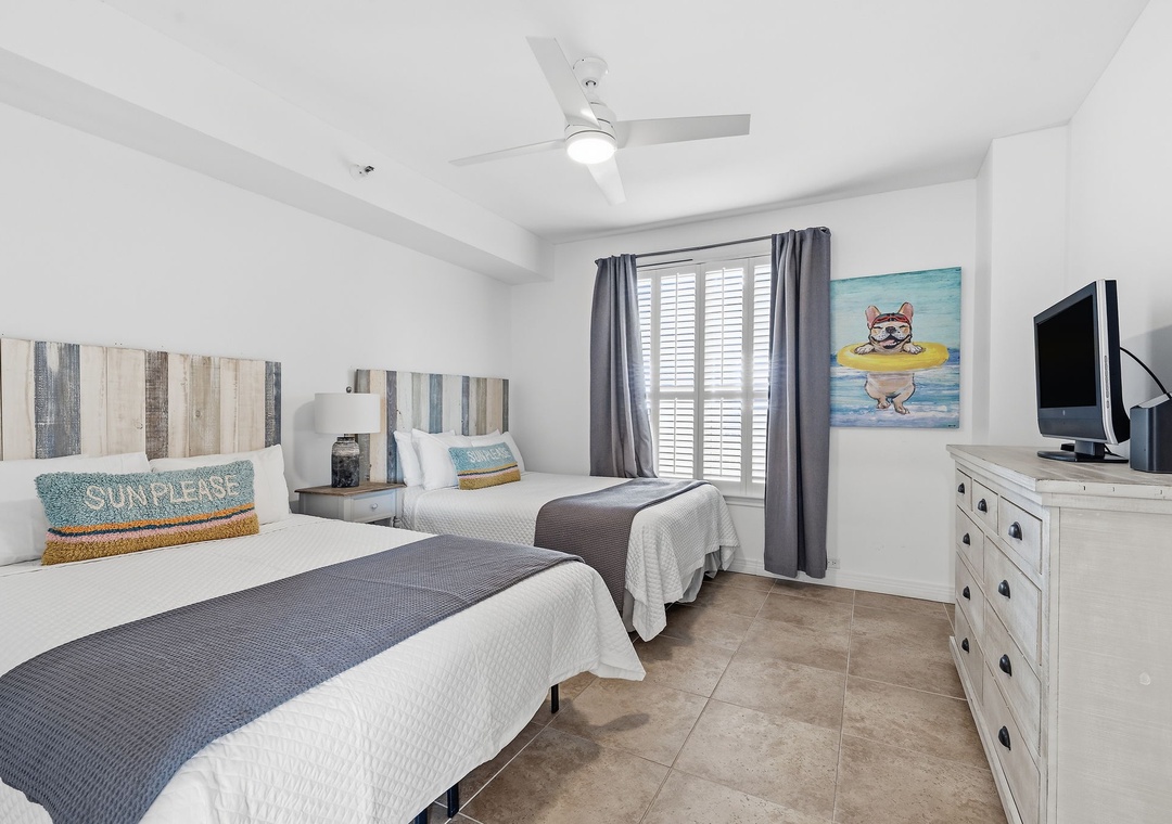 Beach Colony T14B- Unwind in your coastal-inspired guest room, where two plush beds, beach-themed art, and a ceiling fan create a breezy, relaxing retreat perfect for restful nights.