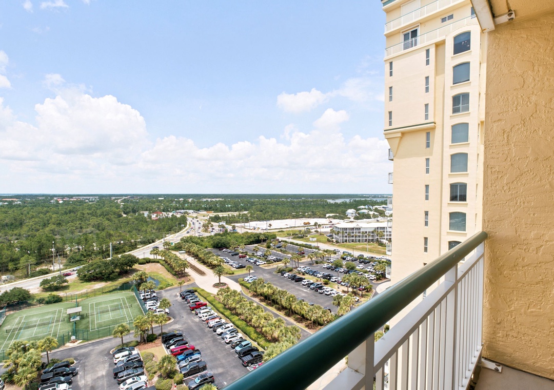 Beach Colony W13A- Elevated view showcasing the property's location with parking areas, tennis courts, and surrounding natural landscape under clear daytime skies.