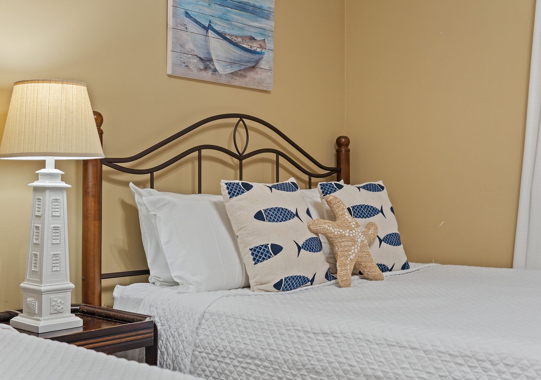 Beach Colony T15B- Sink into crisp white bedding accented with coastal blue fish pillows and a playful starfish, perfect for your seaside getaway dreams.