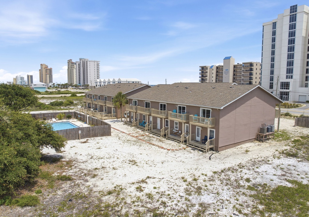 North Lost Key Landing B2- Two-story beachside property with private balconies and pool, nestled between coastal dunes and bay views, surrounded by nearby high-rise buildings.