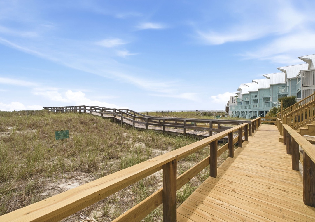 Beachfront property featuring a wooden boardwalk leading through natural dunes to the shore, with direct beach access and coastal architecture in a serene setting.