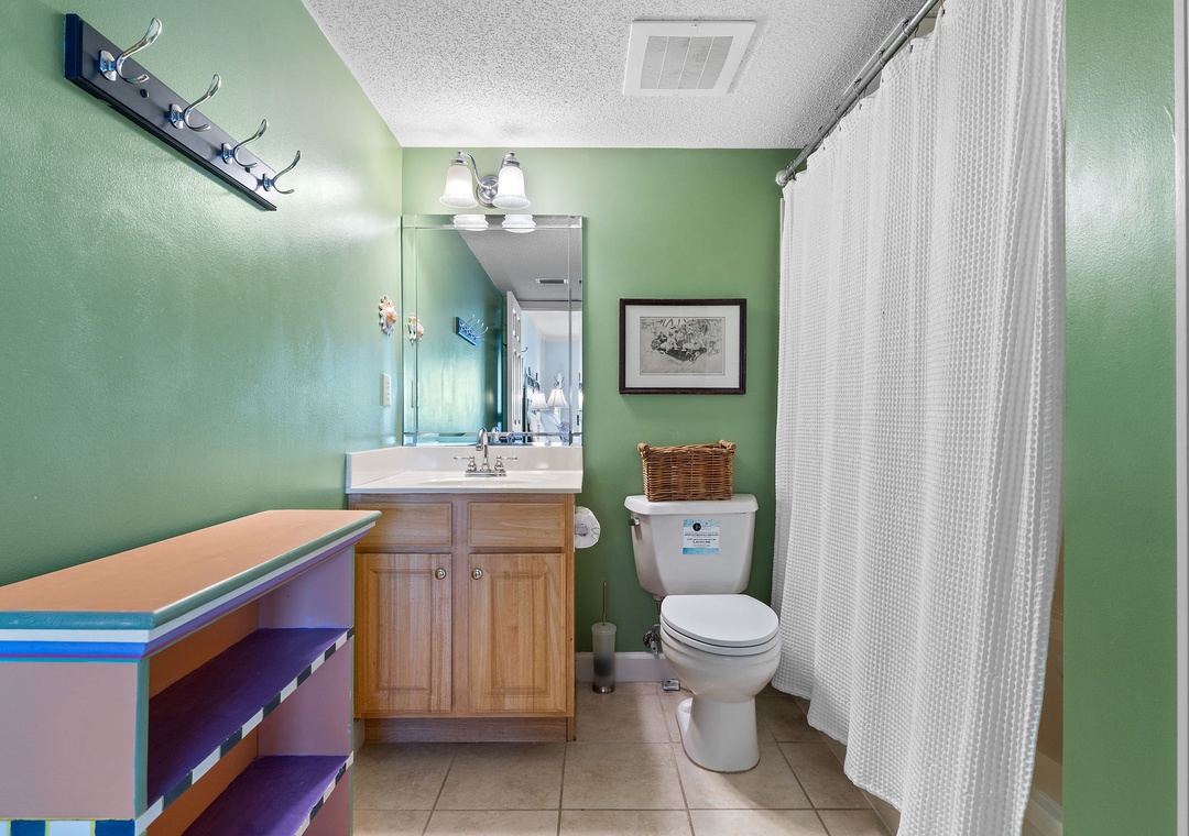 Sandy Key 338- Step into your private bathroom with calming green walls, bright vanity lighting, and a refreshing shower behind the textured curtain. The coastal artwork and thoughtful details make freshening up feel like a mini retreat.