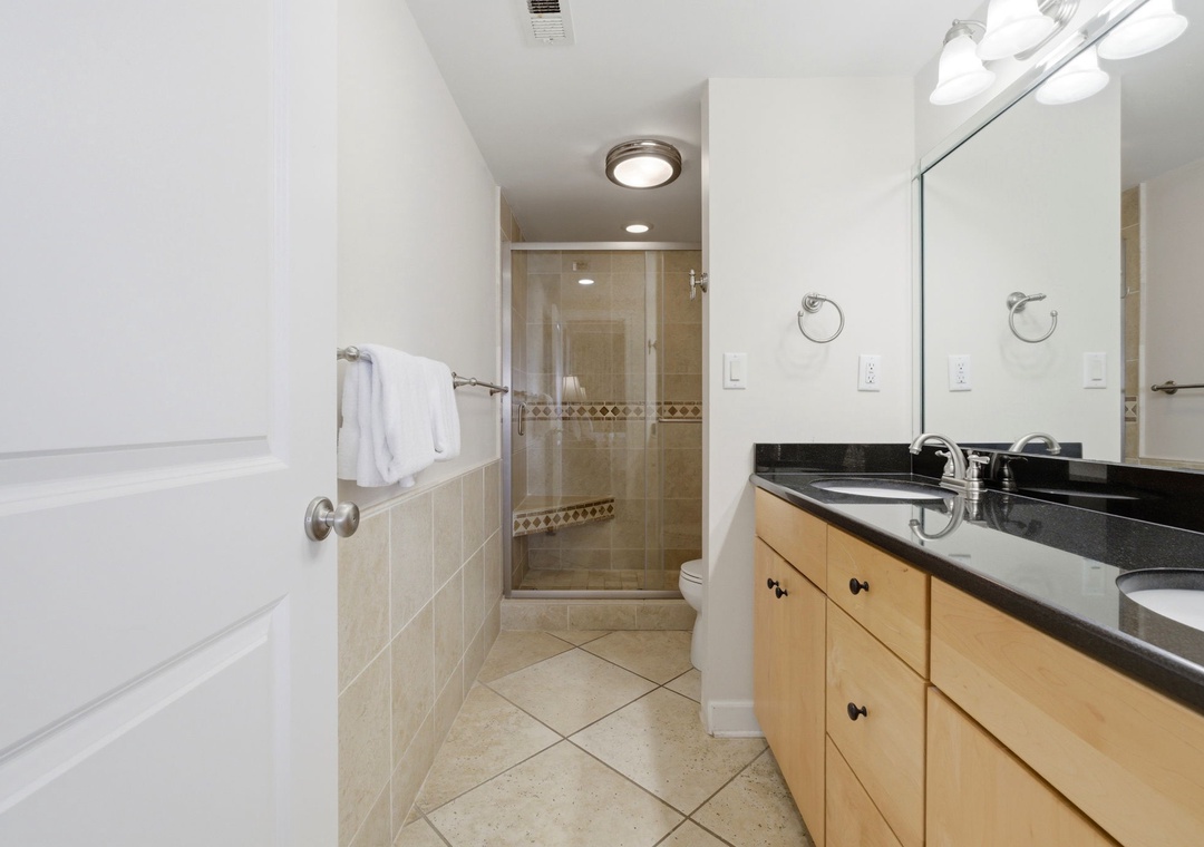 Shipwatch D803- Your private bathroom features a sleek dual-sink vanity with elegant black granite countertops, a walk-in tile shower with modern fixtures, and fresh white towels awaiting your arrival.